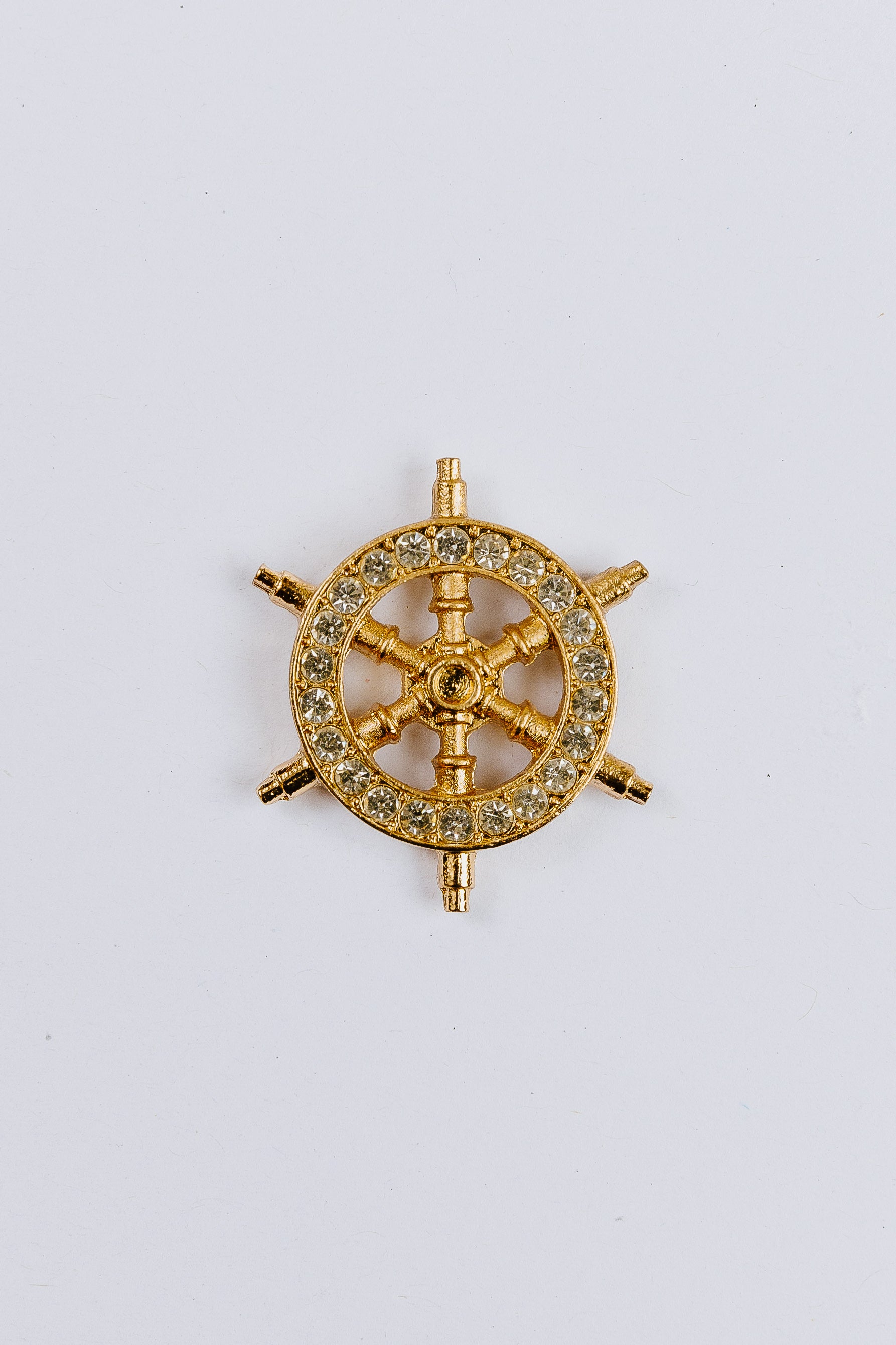Gold steering wheel-shaped charm with gemstones on a white background