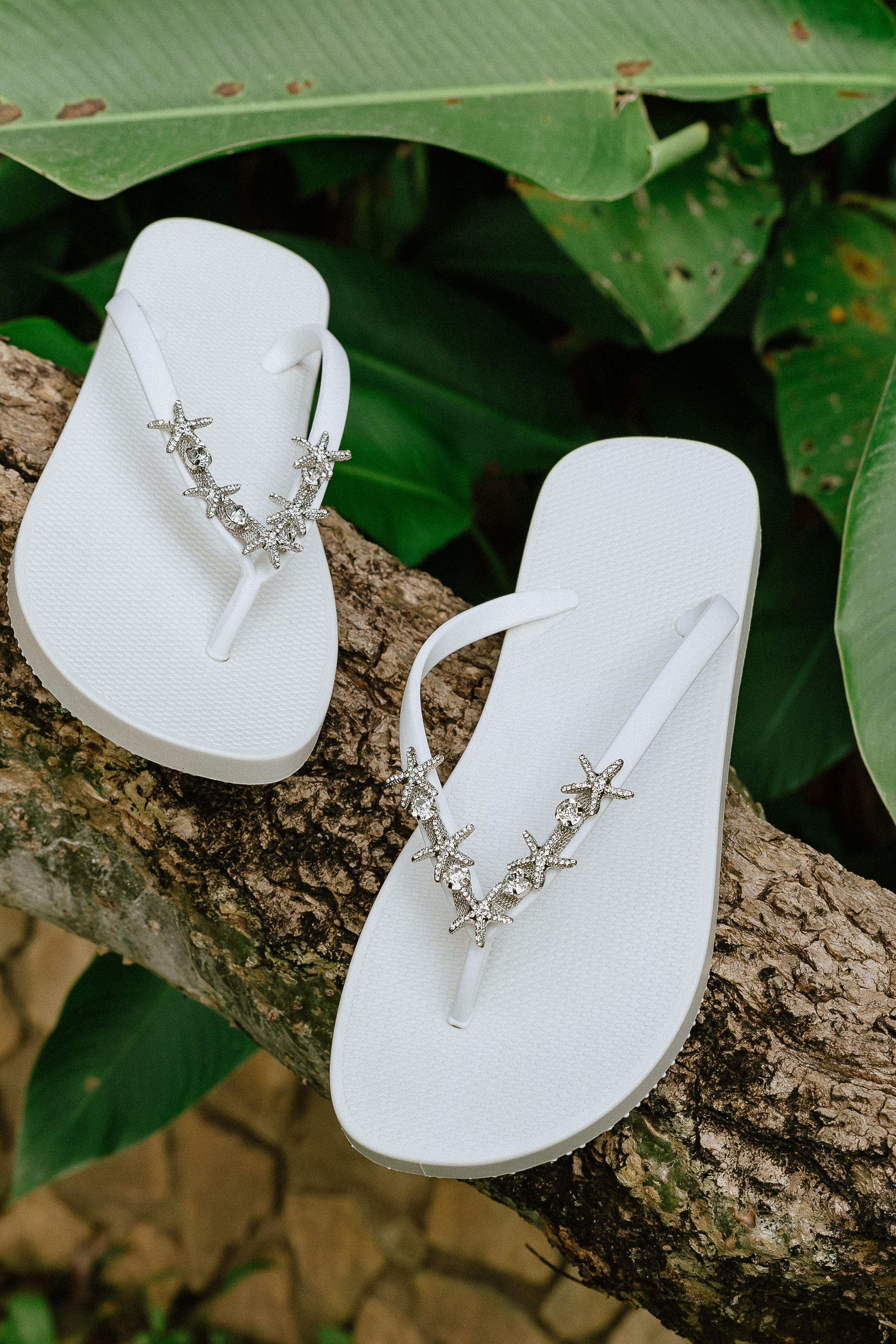 a pair of white flip-flops with a starfish arch-shaped charm with rhinestones in silver