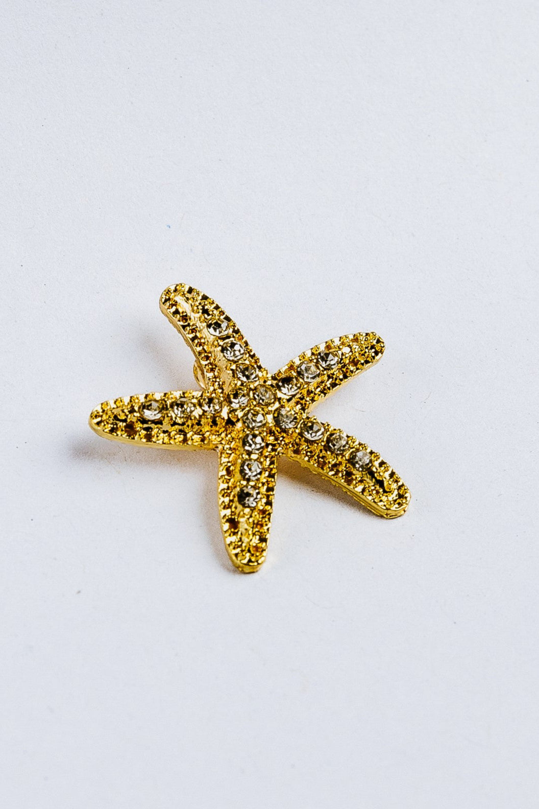 Gold starfish-shaped brooch with rhinestones on a white background