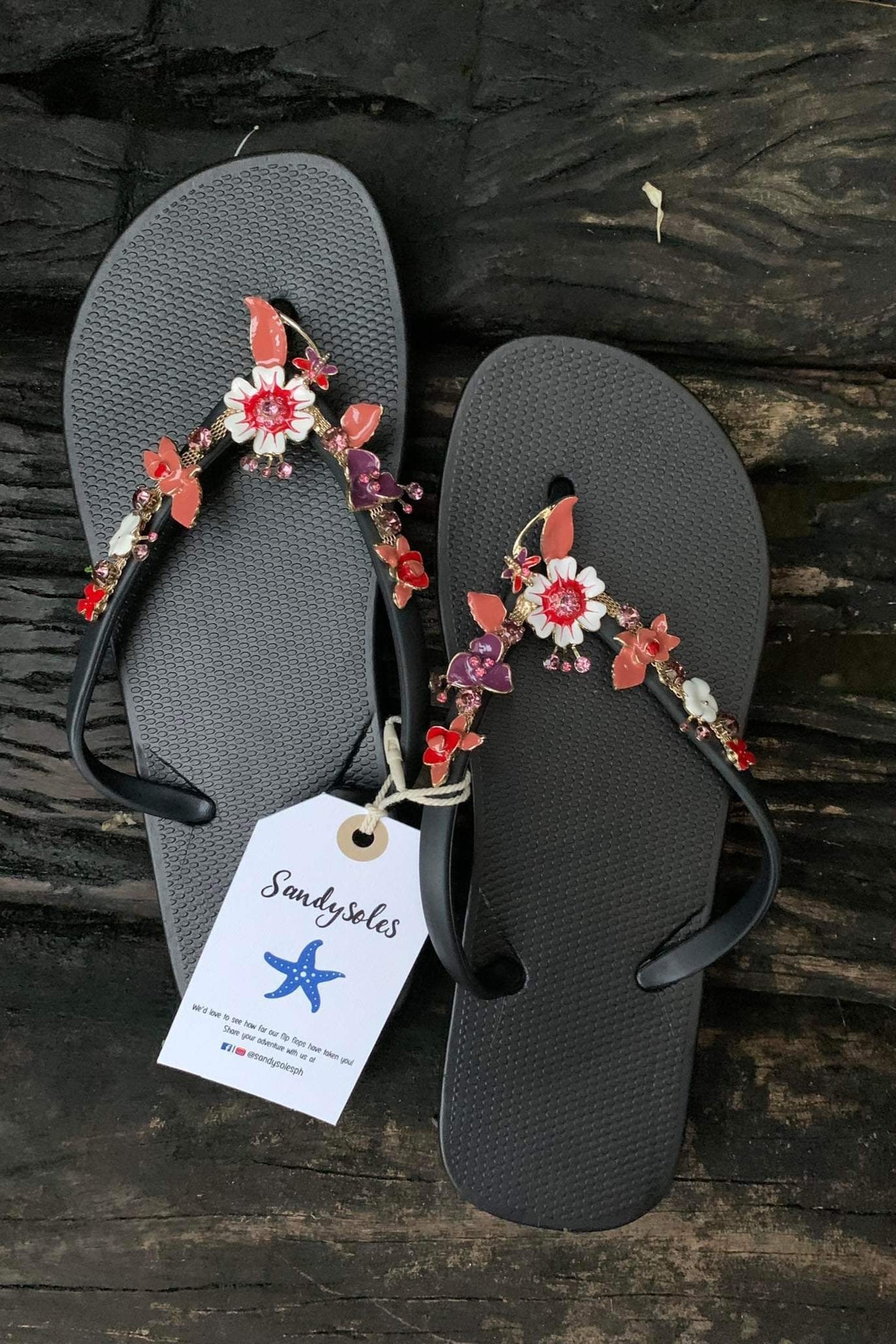 a pair of black flipflops with red flower arch design charm with rhinestones
