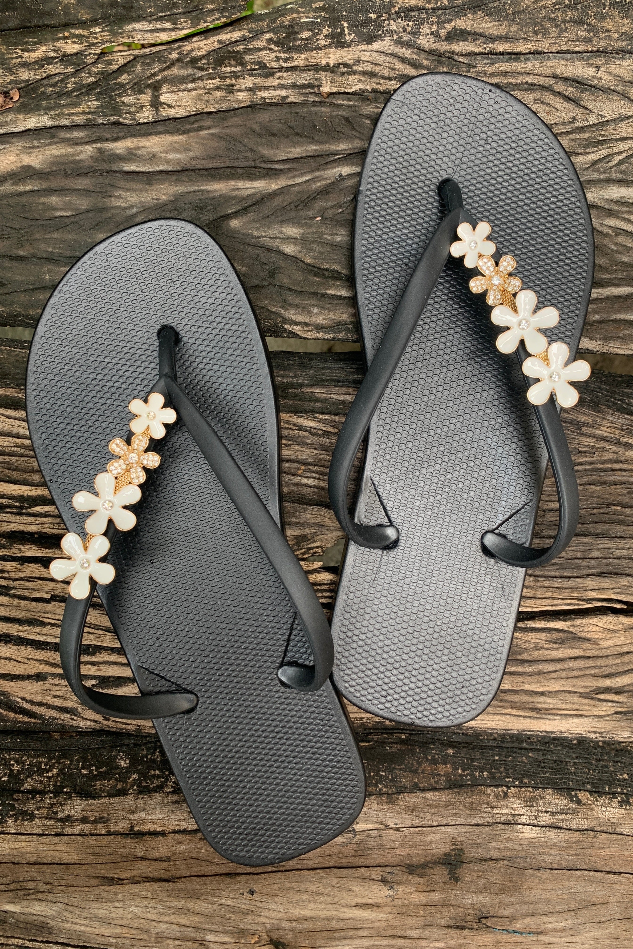 a pair of black flipflops with white flowers as decorative charms