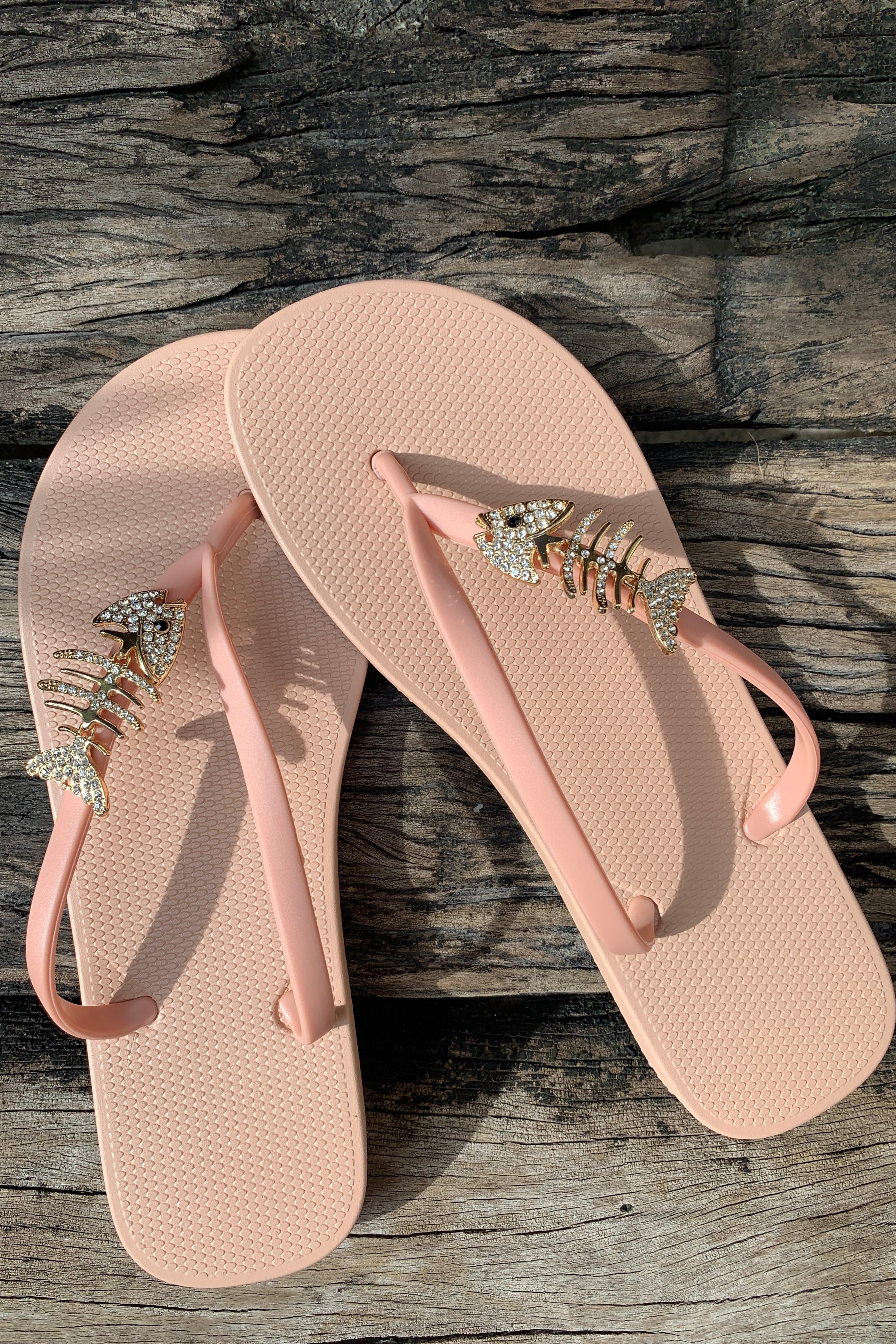 Pink and beige flip-flops with decorative fishbone charm on straps