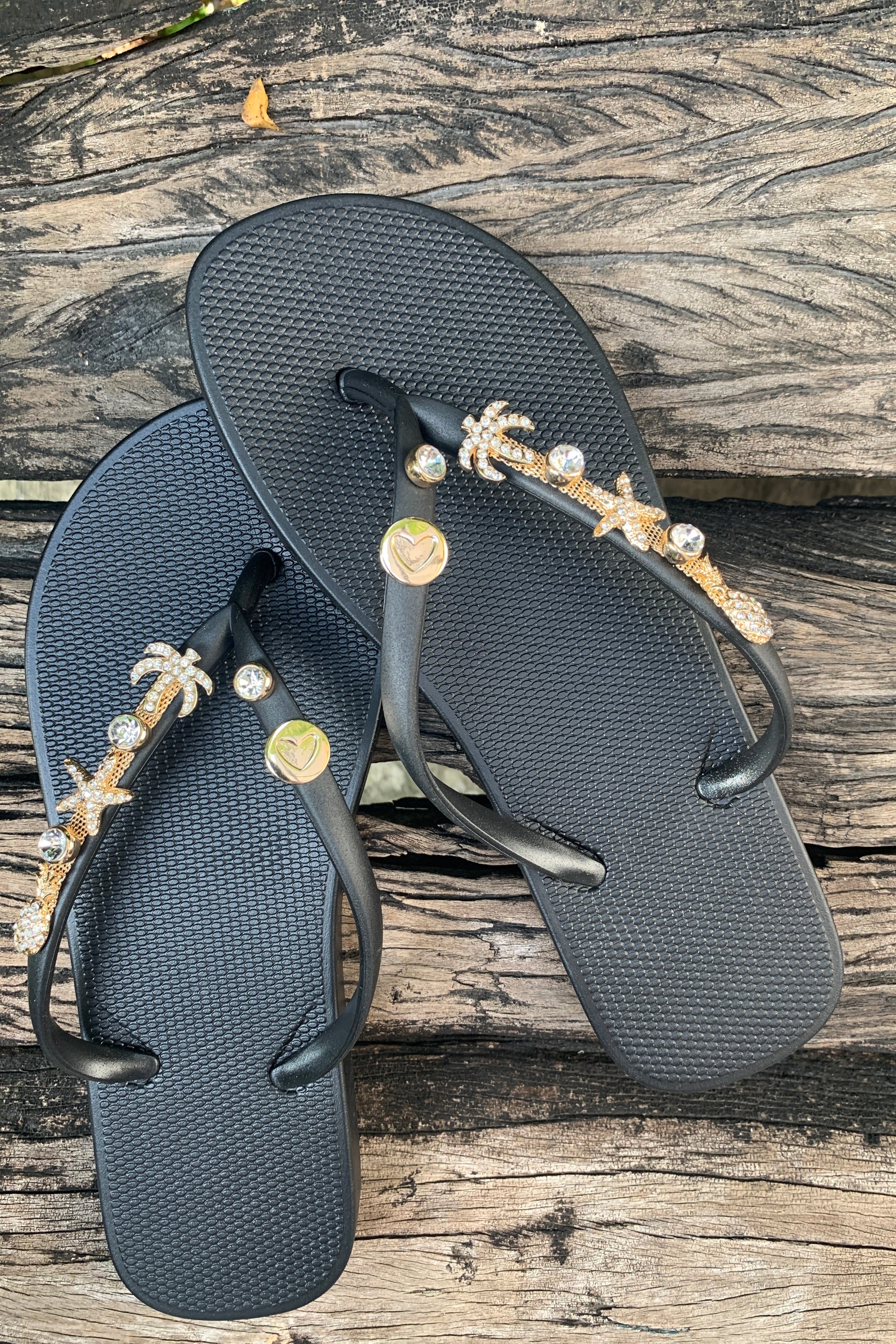 A pair o black flip-flops with heart stud and tropic charms with gemstones