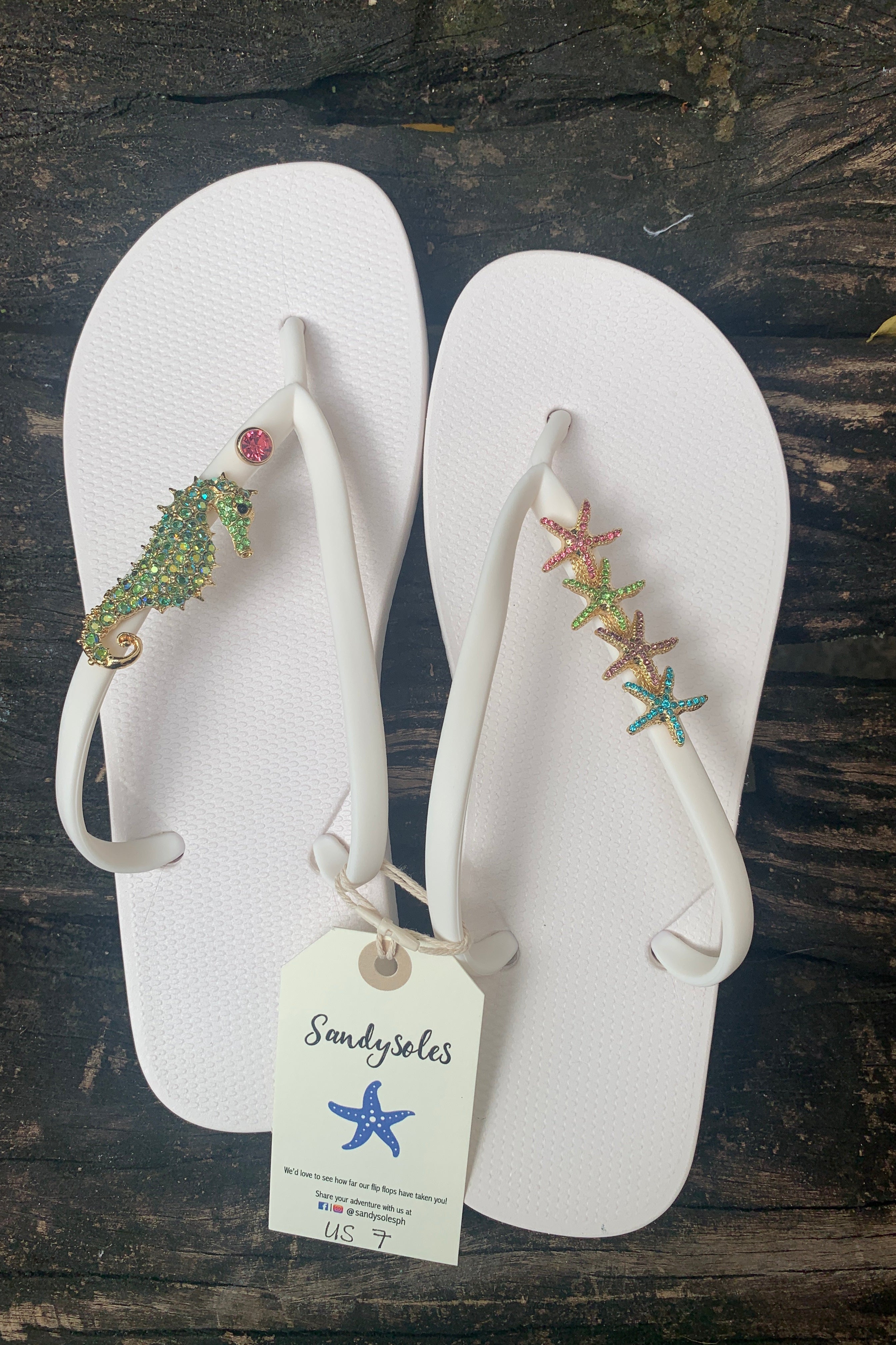 White flip-flops with gemstone, seahorse and starfish charms, featuring a Sandysoles tag