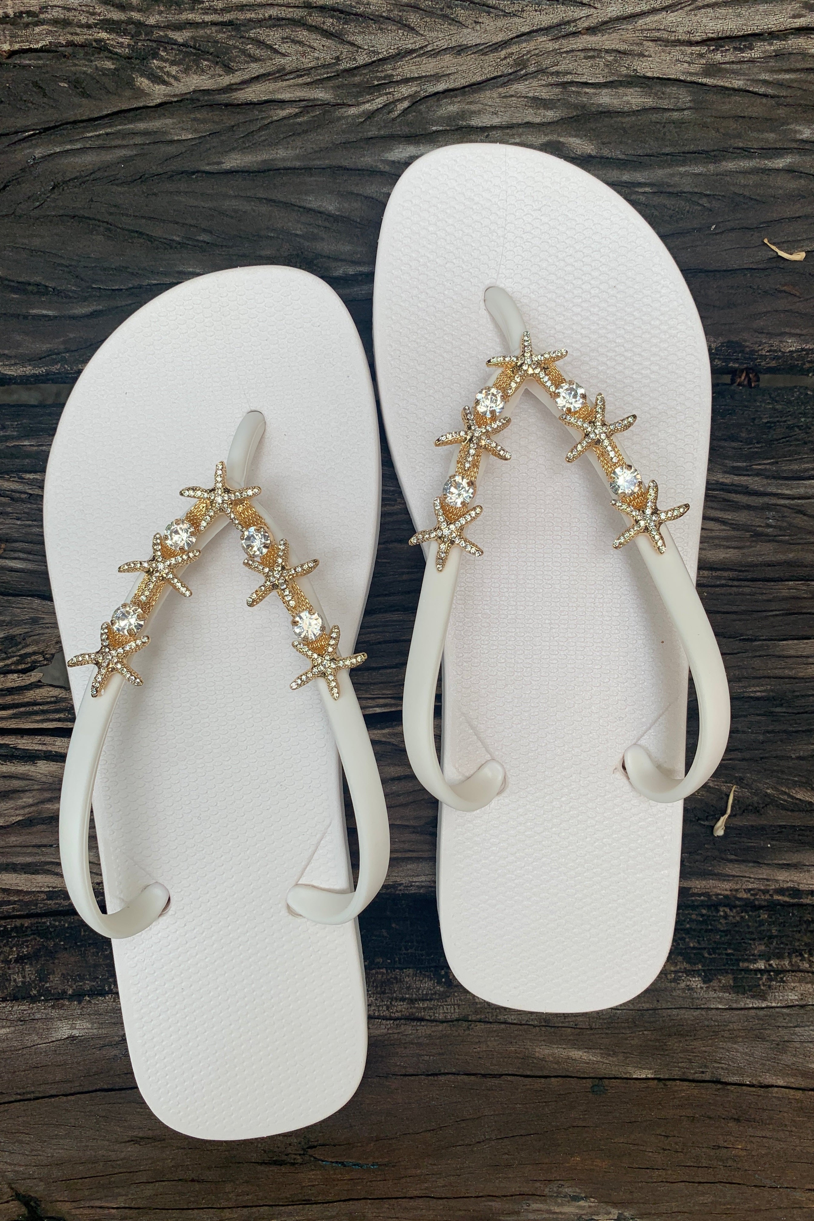 a pair of white flip-flops with a gold twin starfish arch charm