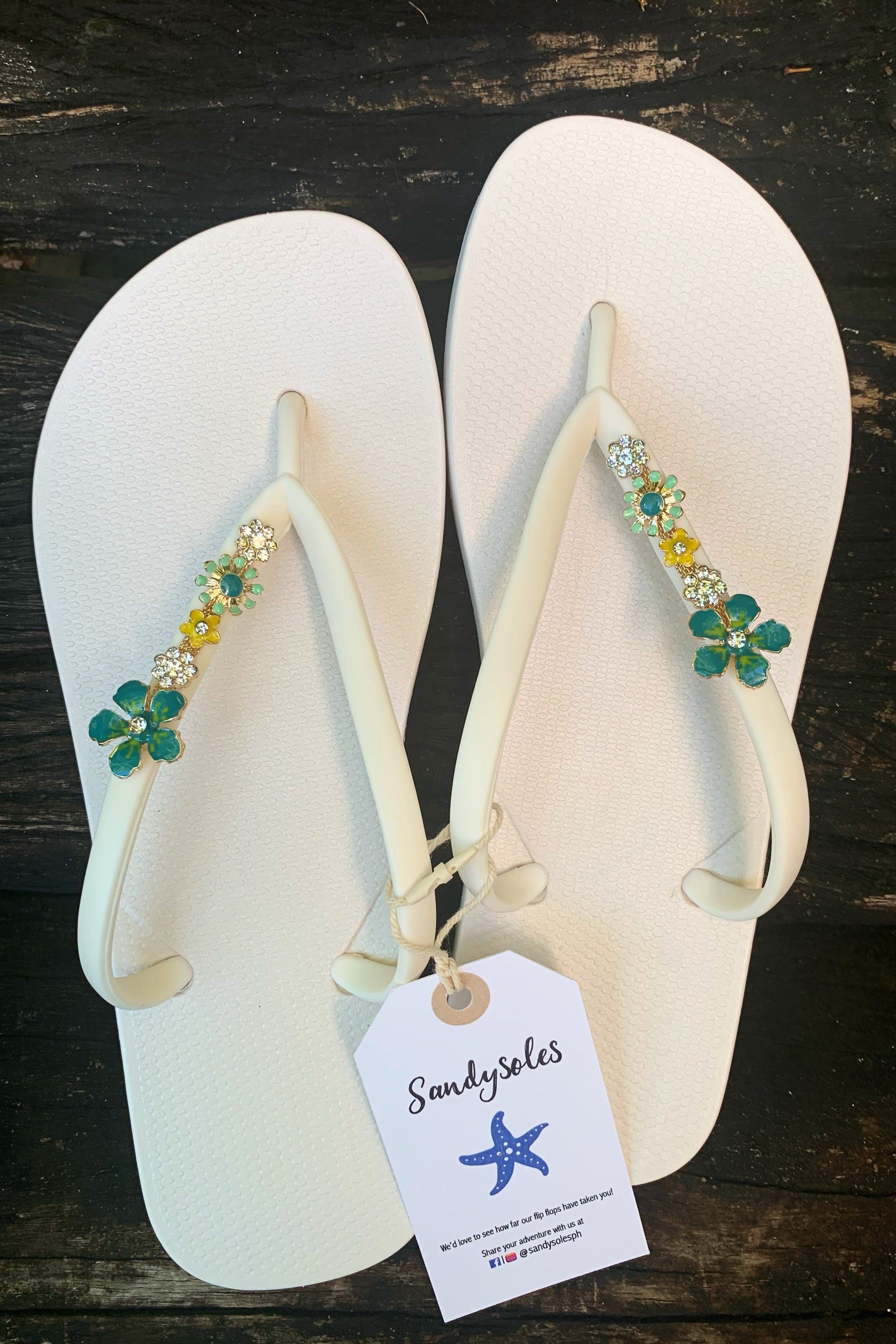 a pair of white flipflops with green flowers as decorative charms