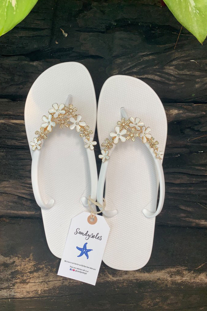 a pair of white flipflops with white flower arch design charm with rhinestones