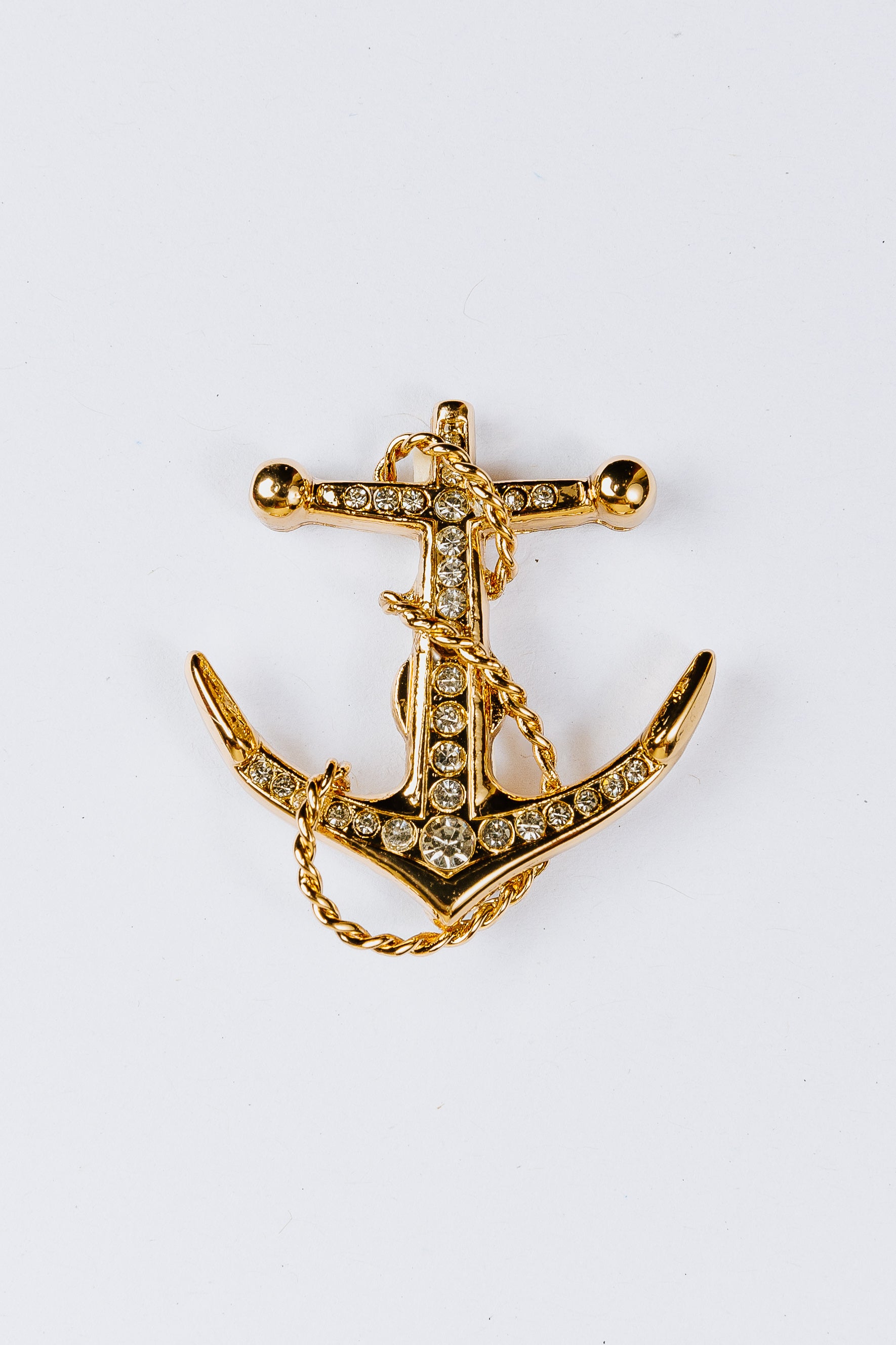 Gold anchor-shaped charm with gemstones on a white background