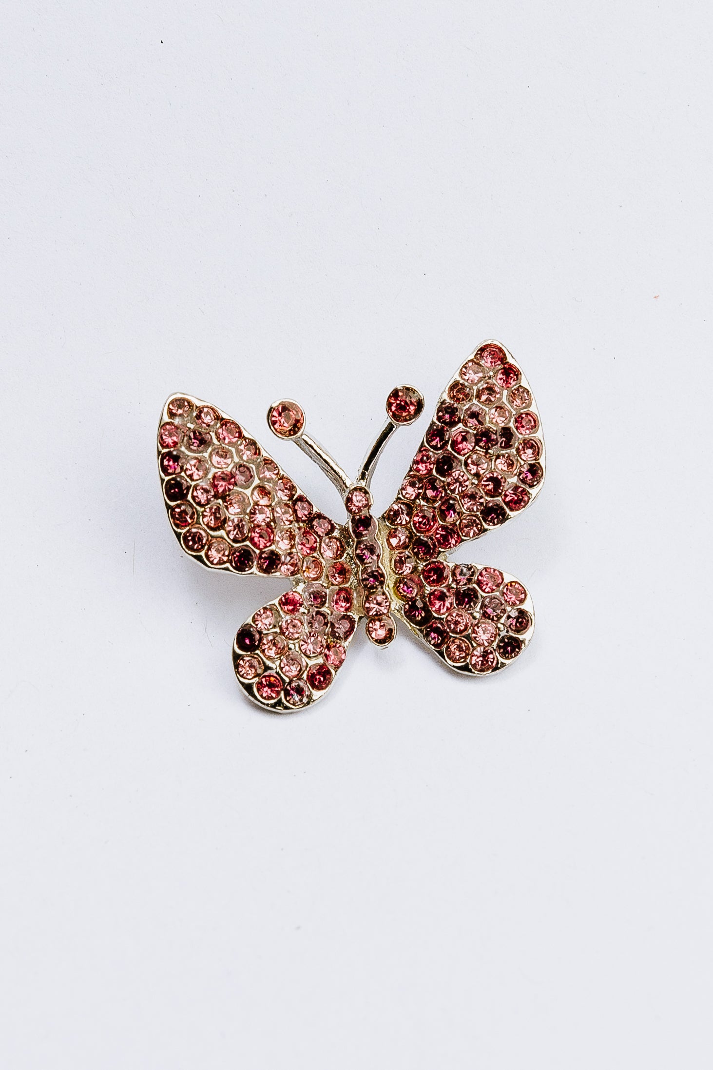 Butterfly-shaped charm with pink gemstones on a white background