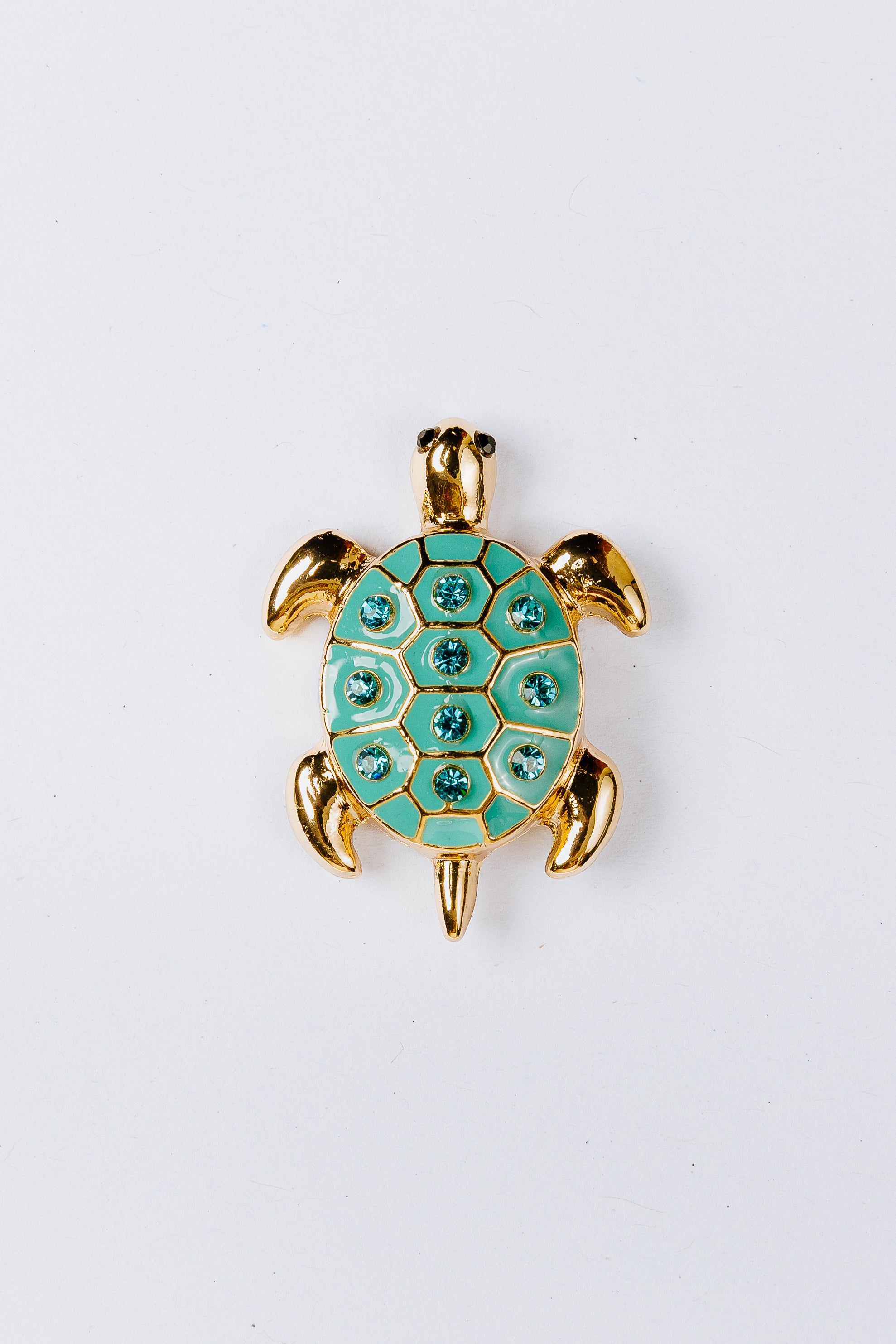 Turtle-shaped charm with green gemstones on a white background