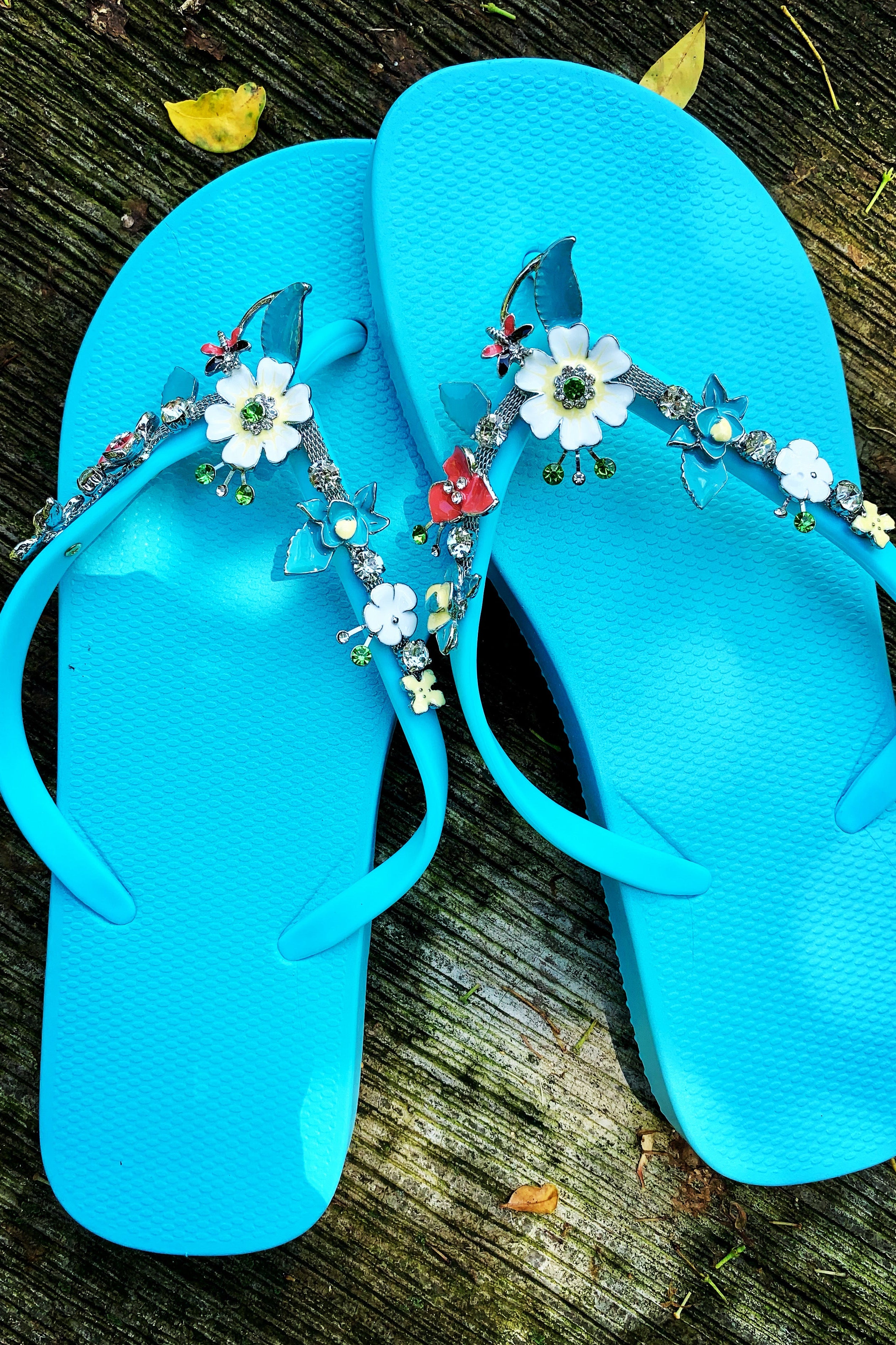 a pair of aqua flipflops with blue flower arch design charm with rhinestones