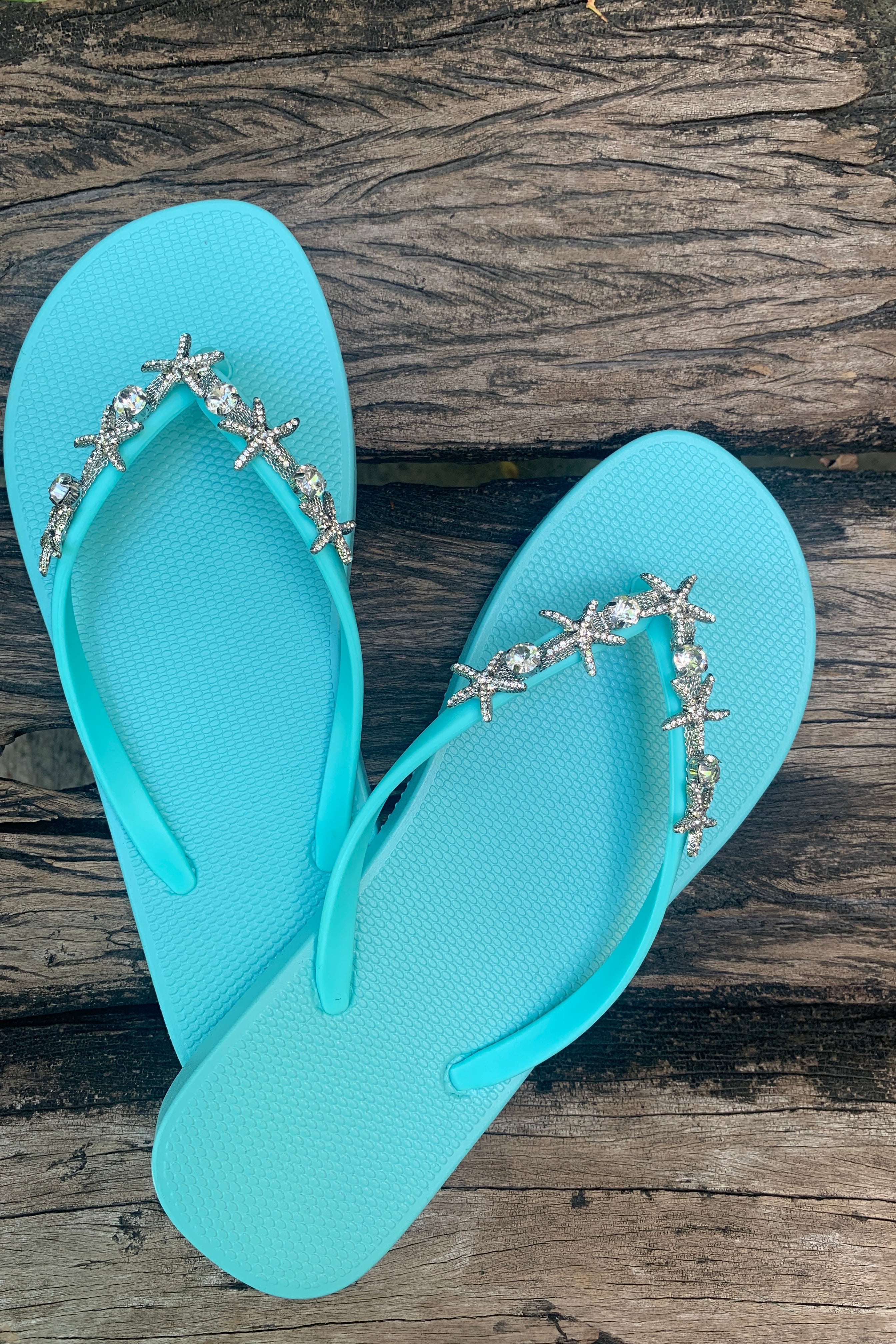 a pair of turquoise flip-flops with a gold starfish arch charm