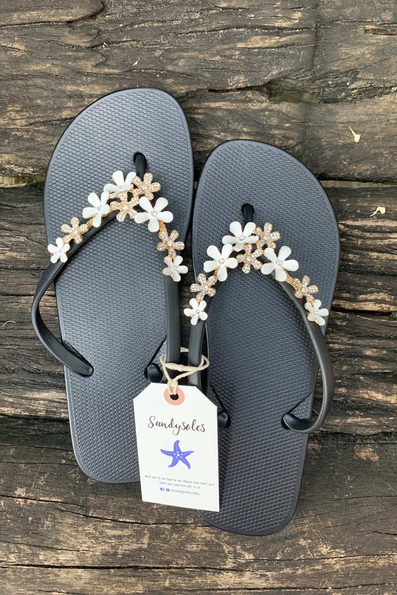 a pair of black flipflops with white flower arch design charm with rhinestones