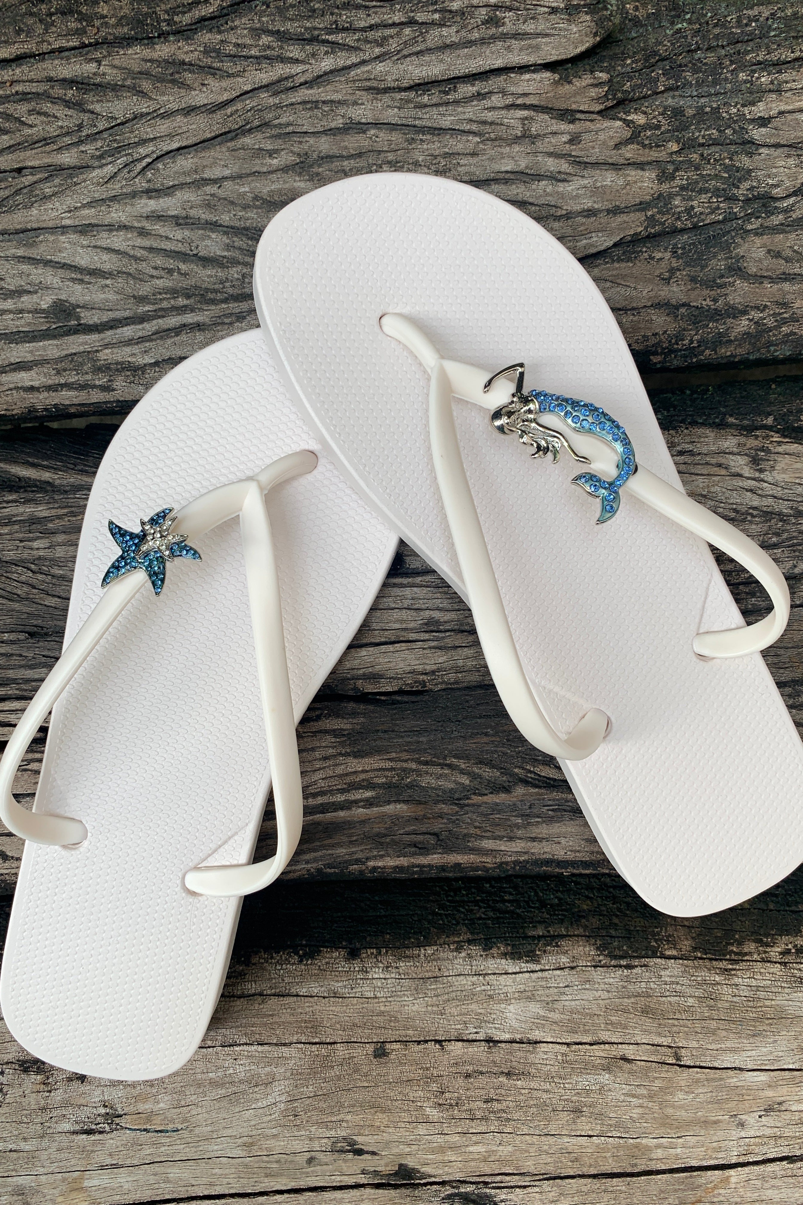 White flip-flops with blue starfish and mermaid charms on straps