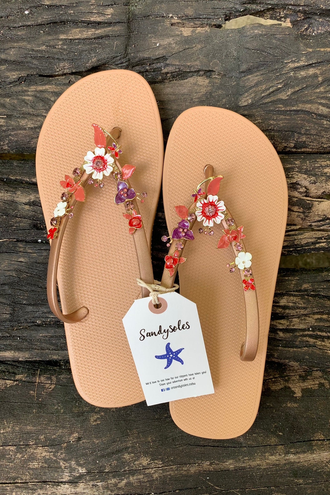 a pair of nude flipflops with red flower arch design charm with rhinestones