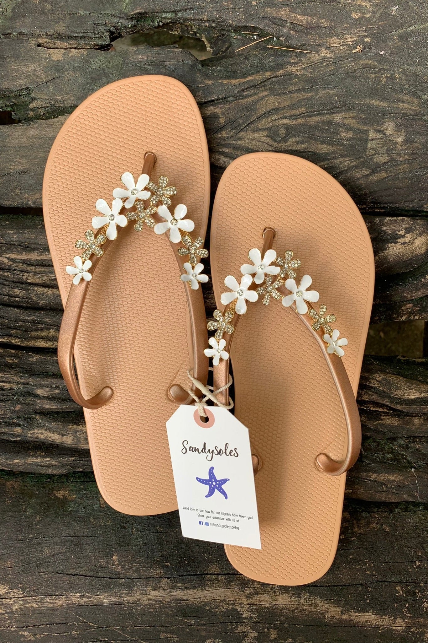 a pair of nude flipflops with white flower arch design charm with rhinestones