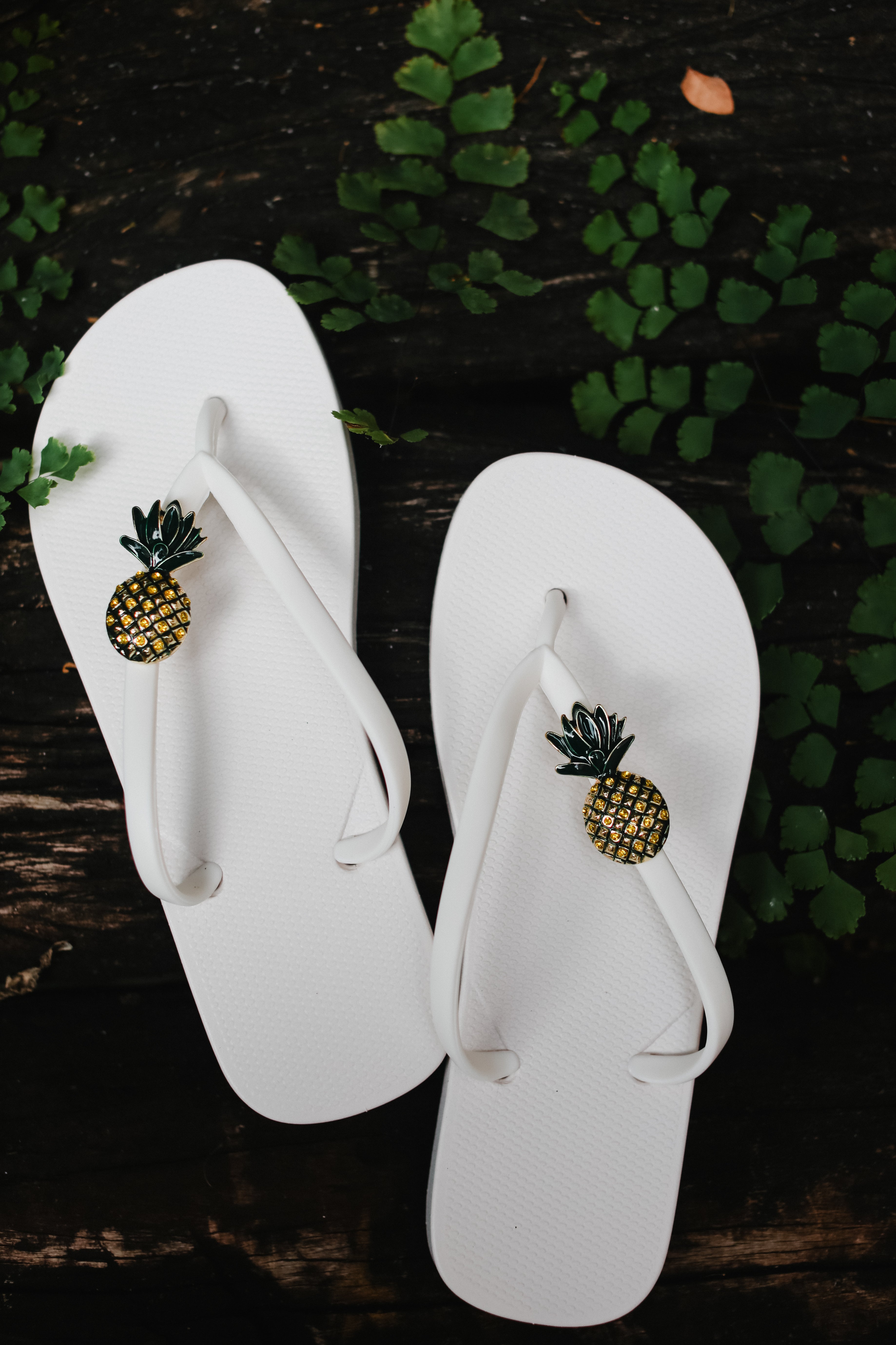 White flip-flops with pineapple embellishments with green leaves.