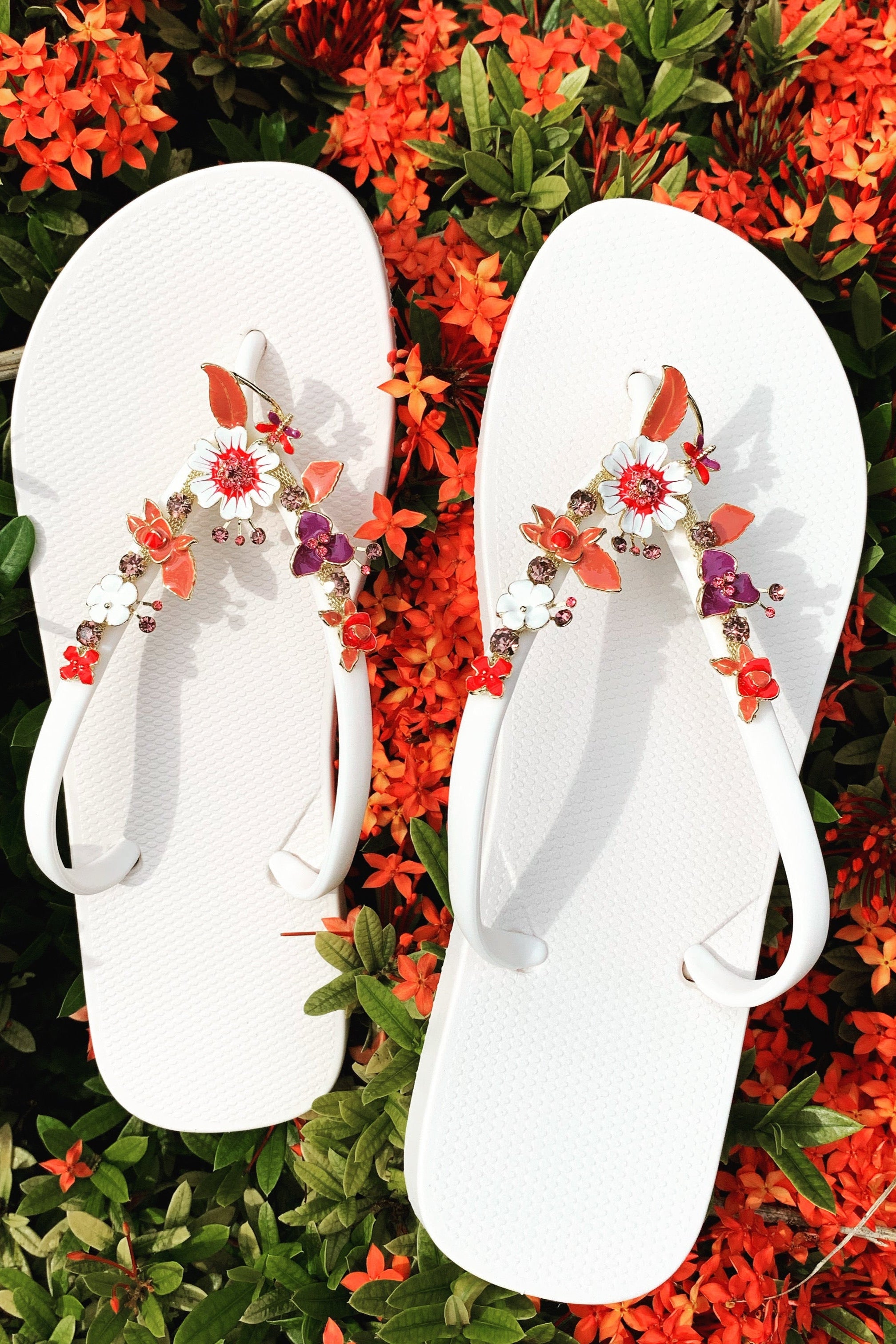 a pair of white flipflops with red flower arch design charm with rhinestones