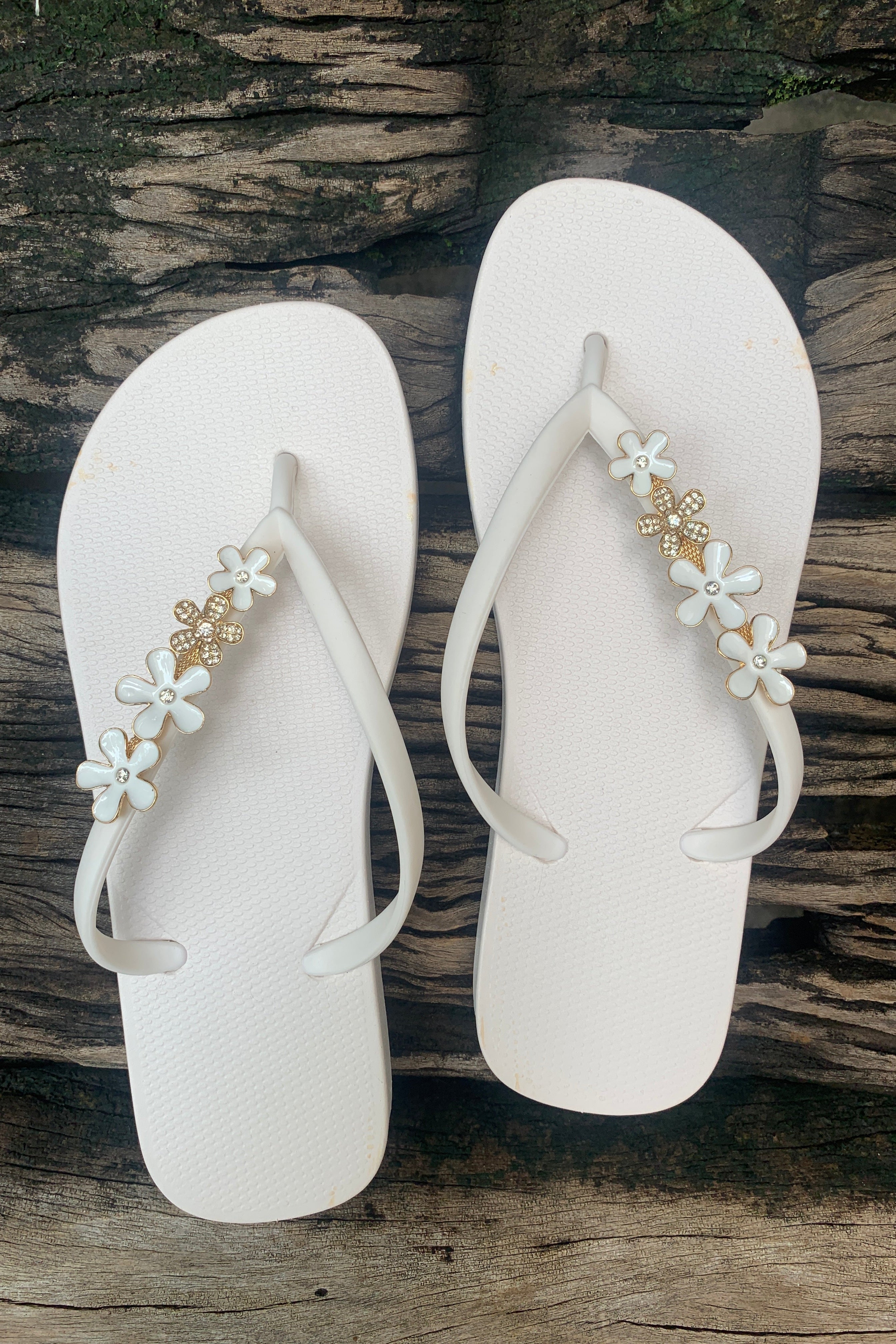 White flip-flops with decorative white floral charms on straps 